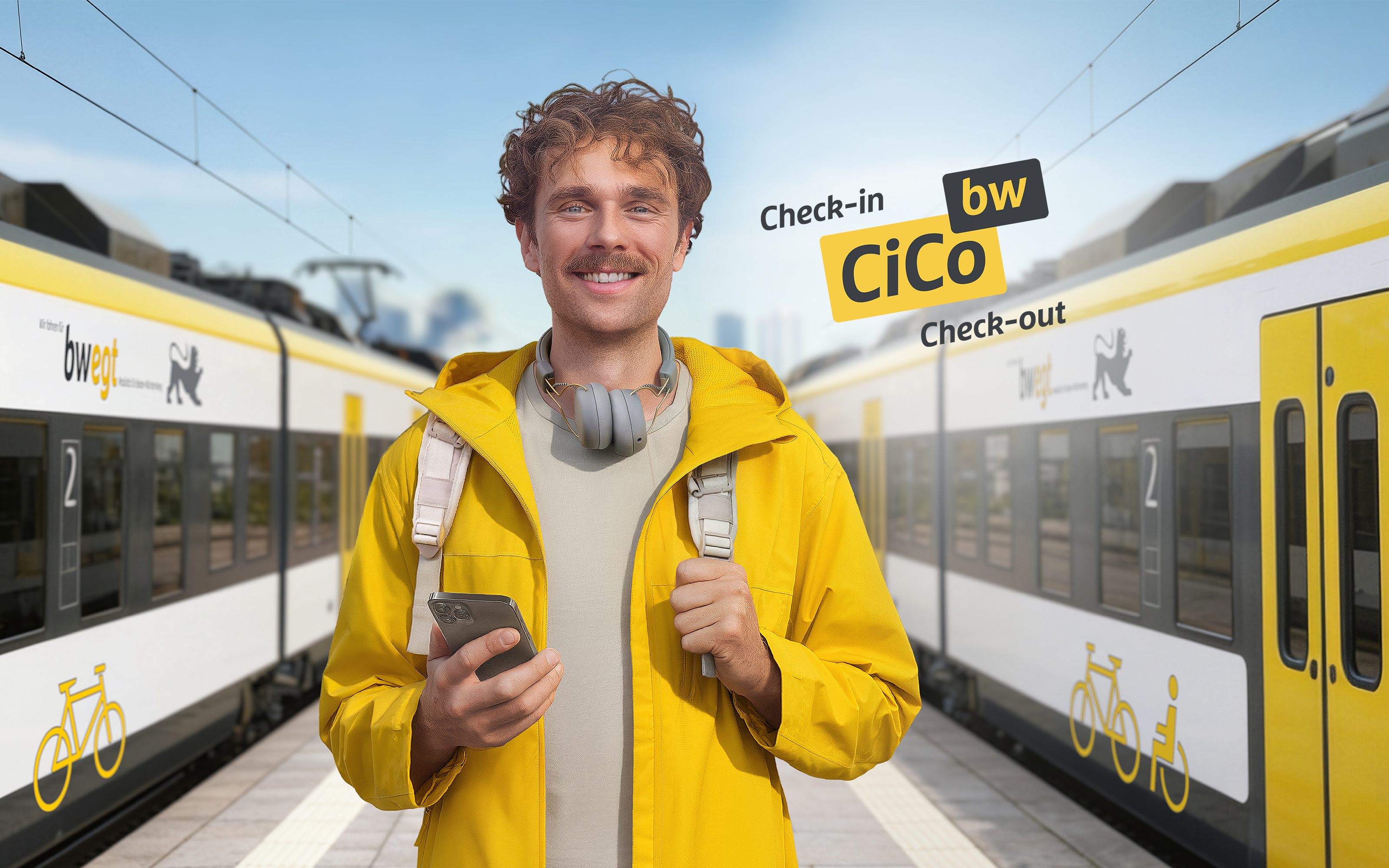 Ein Mann in gelber Kleidung steht mit seinem Handy am Bahnhof. Links und rechts von ihm steht jeweils ein bwegt-Zug.