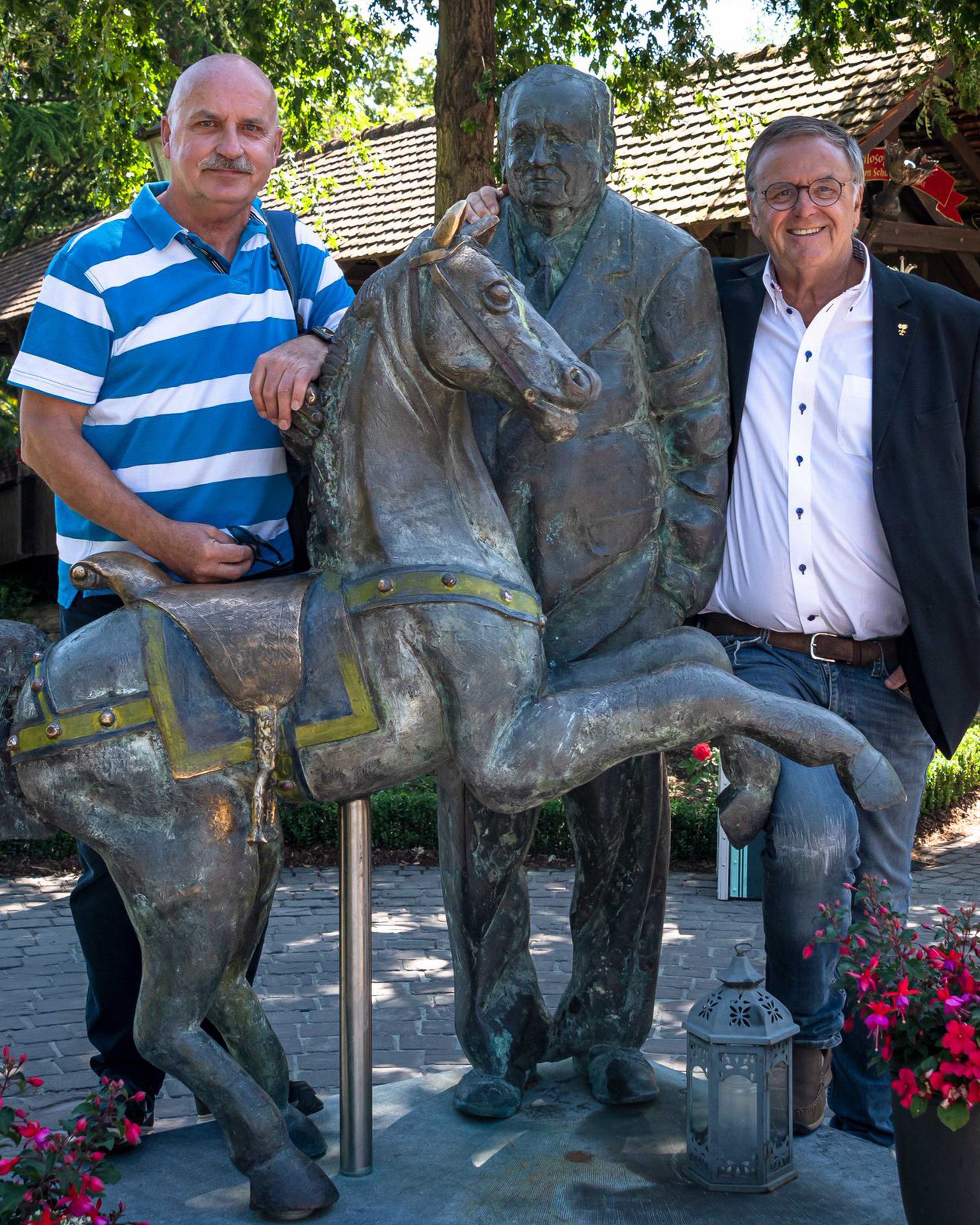 Zwei mittelalte Herren stehen neben einer Statue im Europa-Park. Die Statue zeigt einen alten Mann neben einem Pferd.