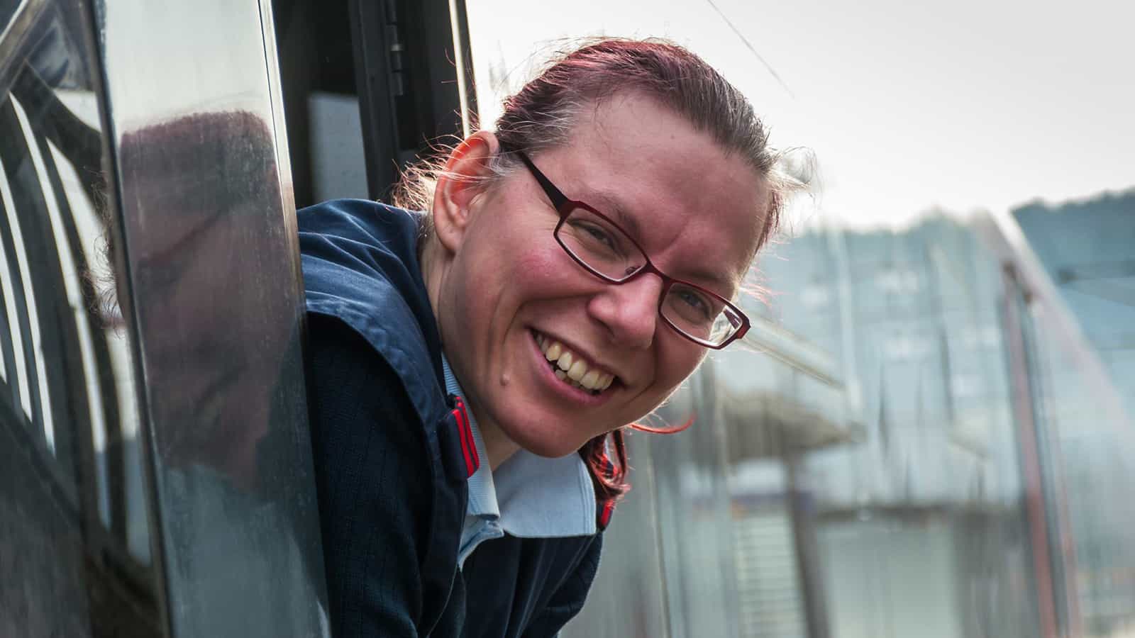 Lokführerin schaut aus dem Fenster eines Zugs und lächelt. 