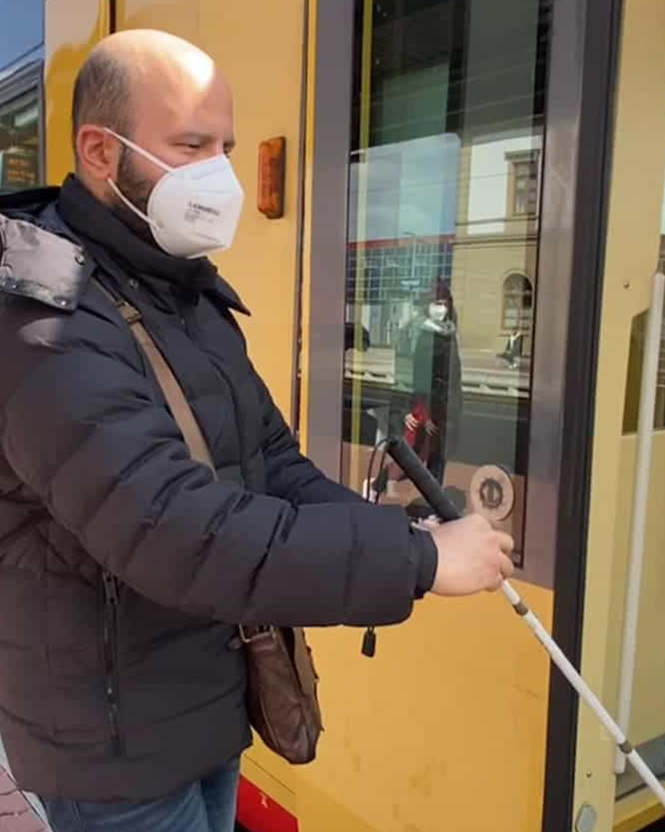 Blinder mit Gehstock öffnet Tür zur Straßenbahn.