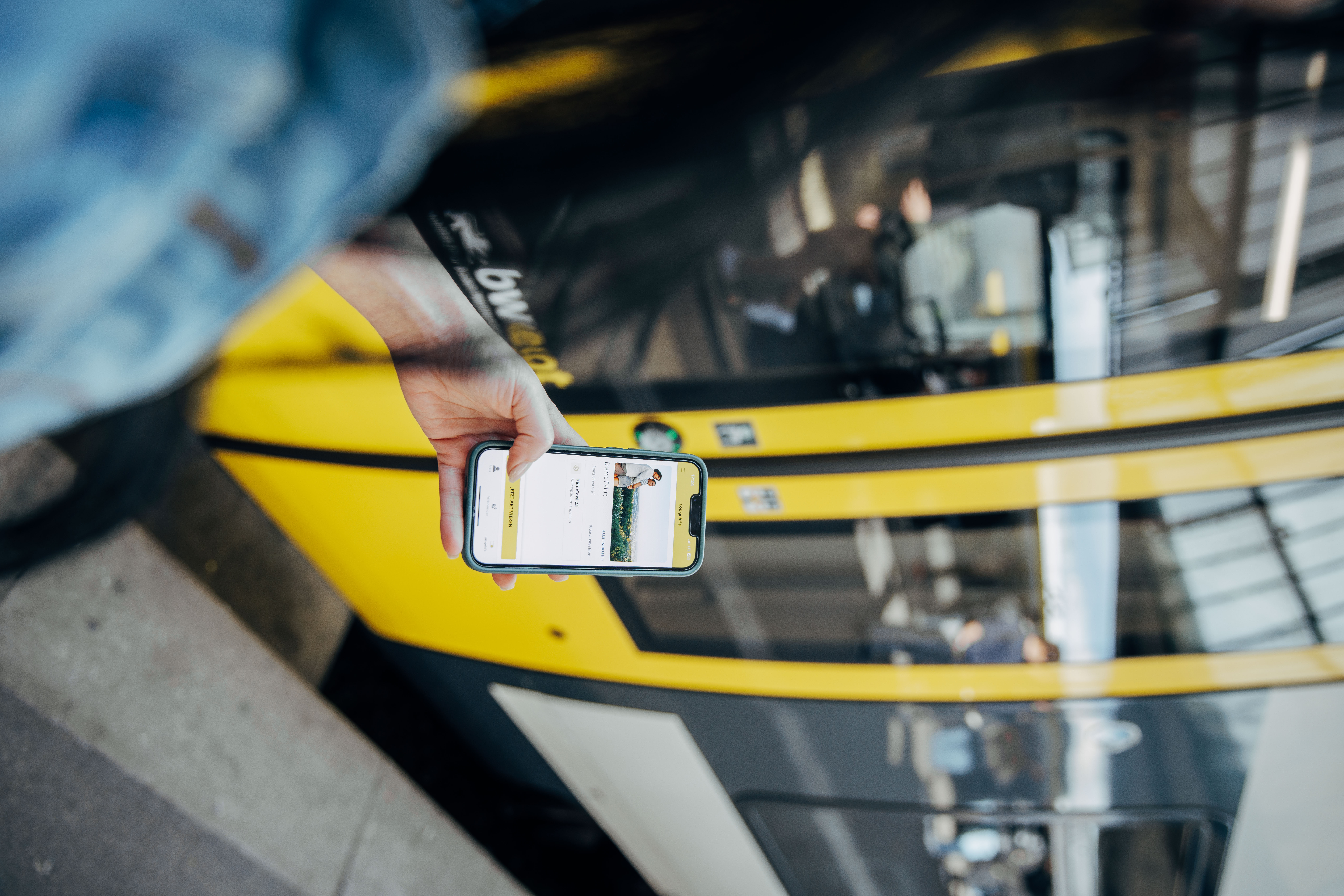 Blick über die Schulter einer Frau auf das Smartphone in der Hand mit Ticket-App. Im Hintergrund steht ein bwegt-Zug.