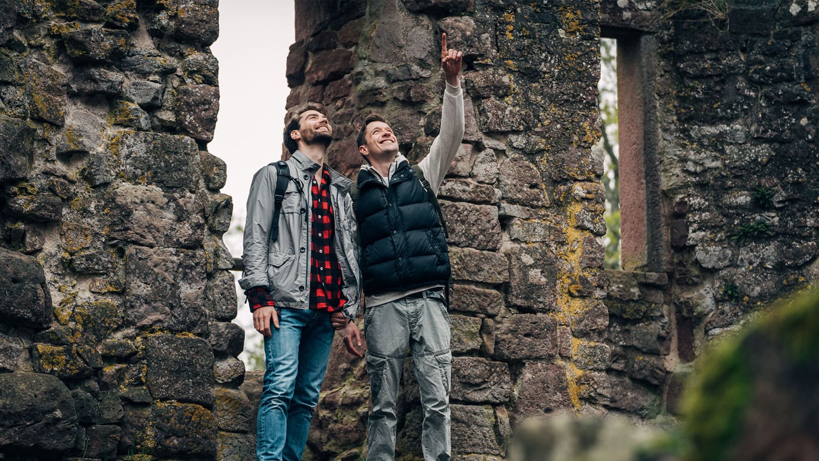 Zwei junge Männer in Wanderkleidung entdecken und bestaunen eine alte Ruine