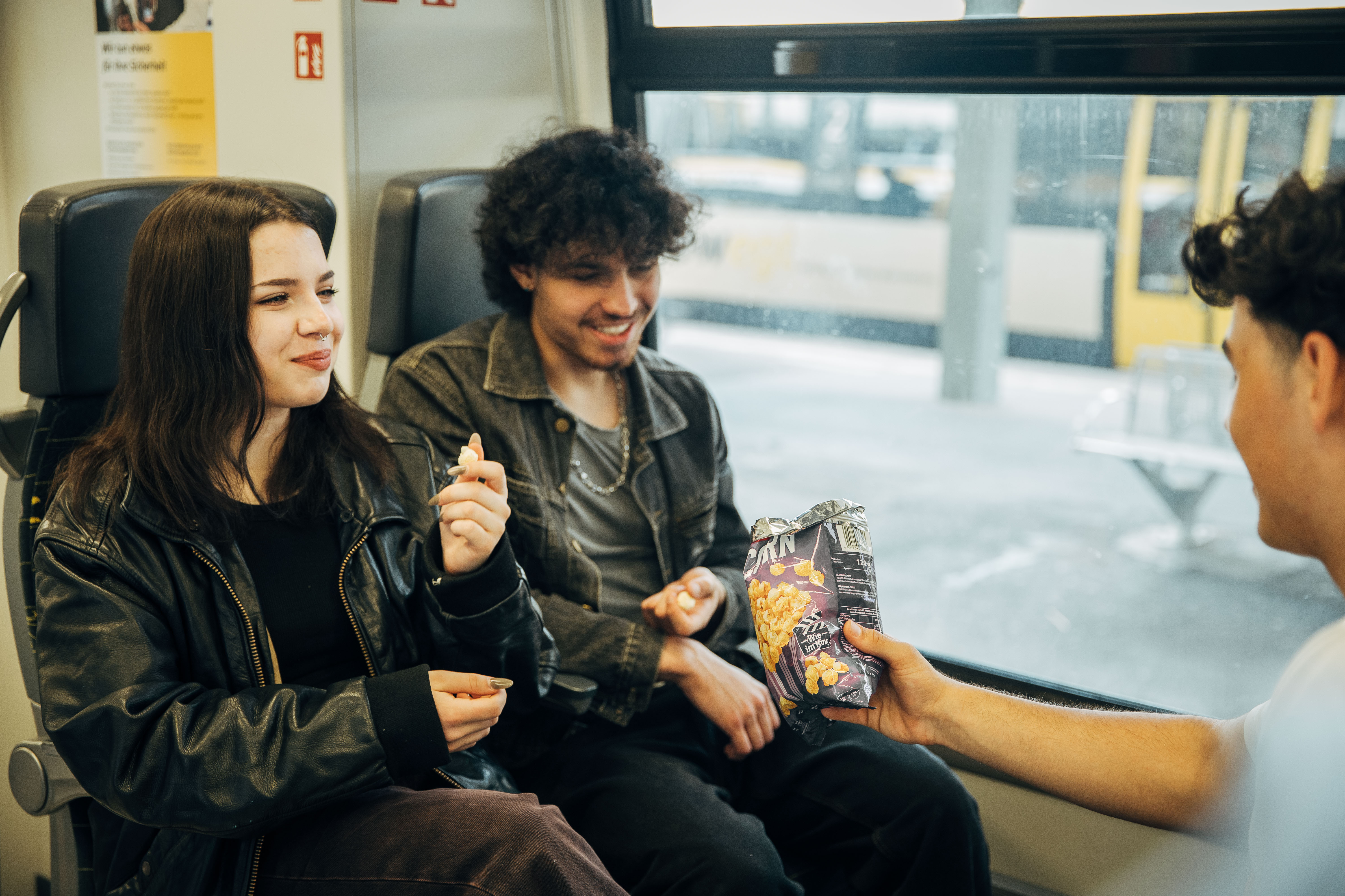 Junge Menschen, die lachend in der Bahn sitzen und Popcorn essen