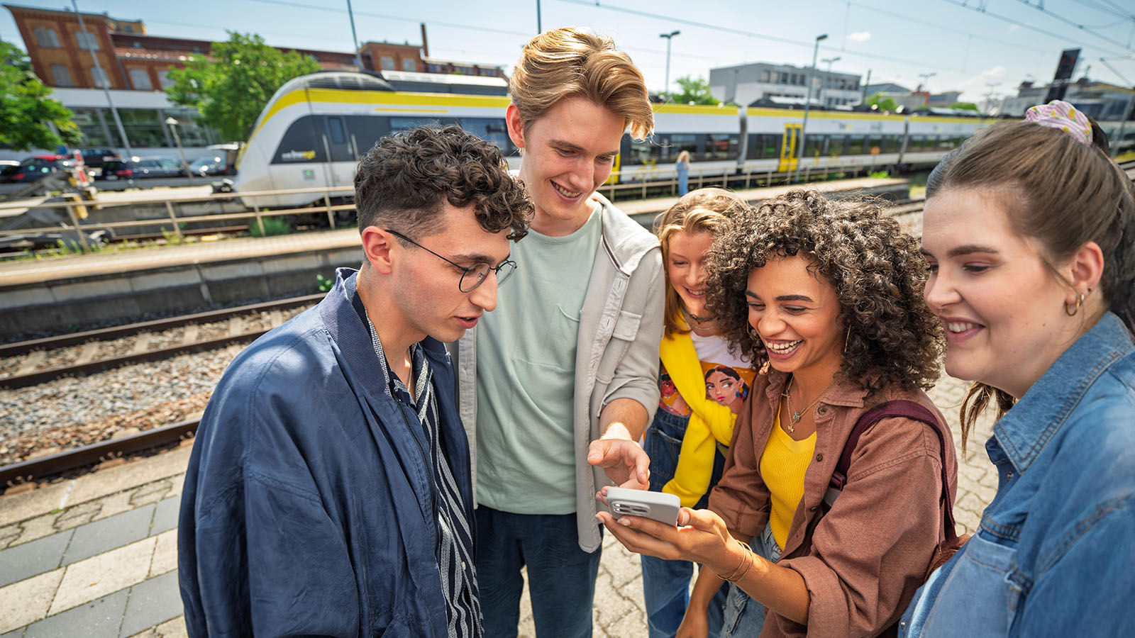 Mehrere Jugendliche stehen am Bahnhof und schauen gemeinsam auf ein Smartphone
