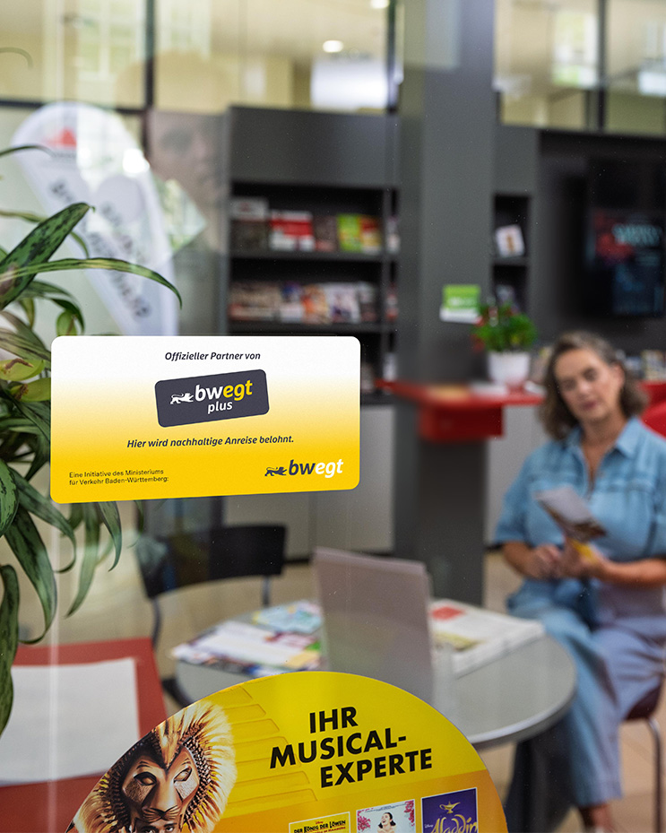 Eine Frau sitzt hinter einem Schaufenster, im Fokus ist ein bwegtPlus-Aufkleber